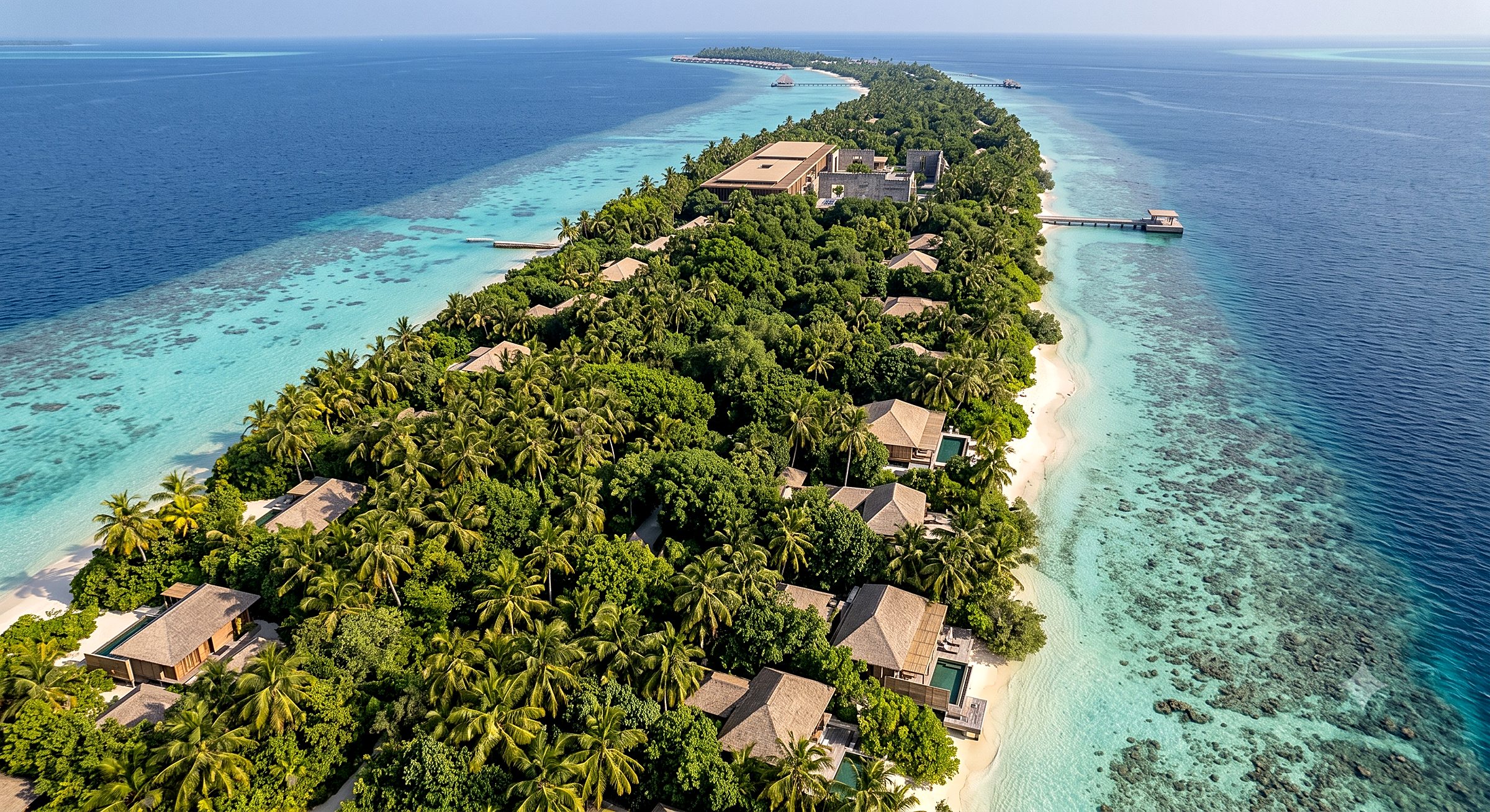 Aerial visualization along the length of Dholhiyadhoo — beach villas with private pools dissolved into regrown vegetation, the Ruin Garden Forum mid-island, piers on the reef edge and overwater villas at the far tip.